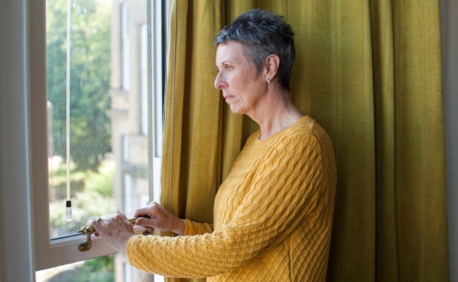 Older woman looking pensively out a window.